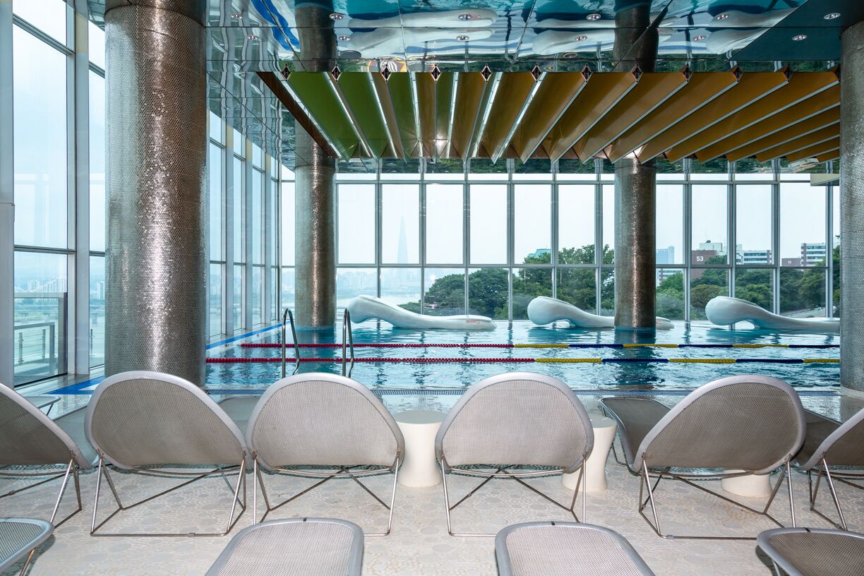 An indoor swimming pool with modern chairs and large windows.