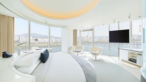 Una habitación de hotel moderna con una cama grande, dos sillones, un televisor y vistas a la ciudad.