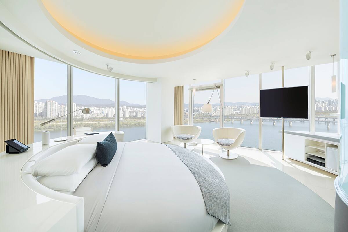 Een moderne hotelkamer met een groot bed, twee fauteuils, een televisie en uitzicht op de stad.