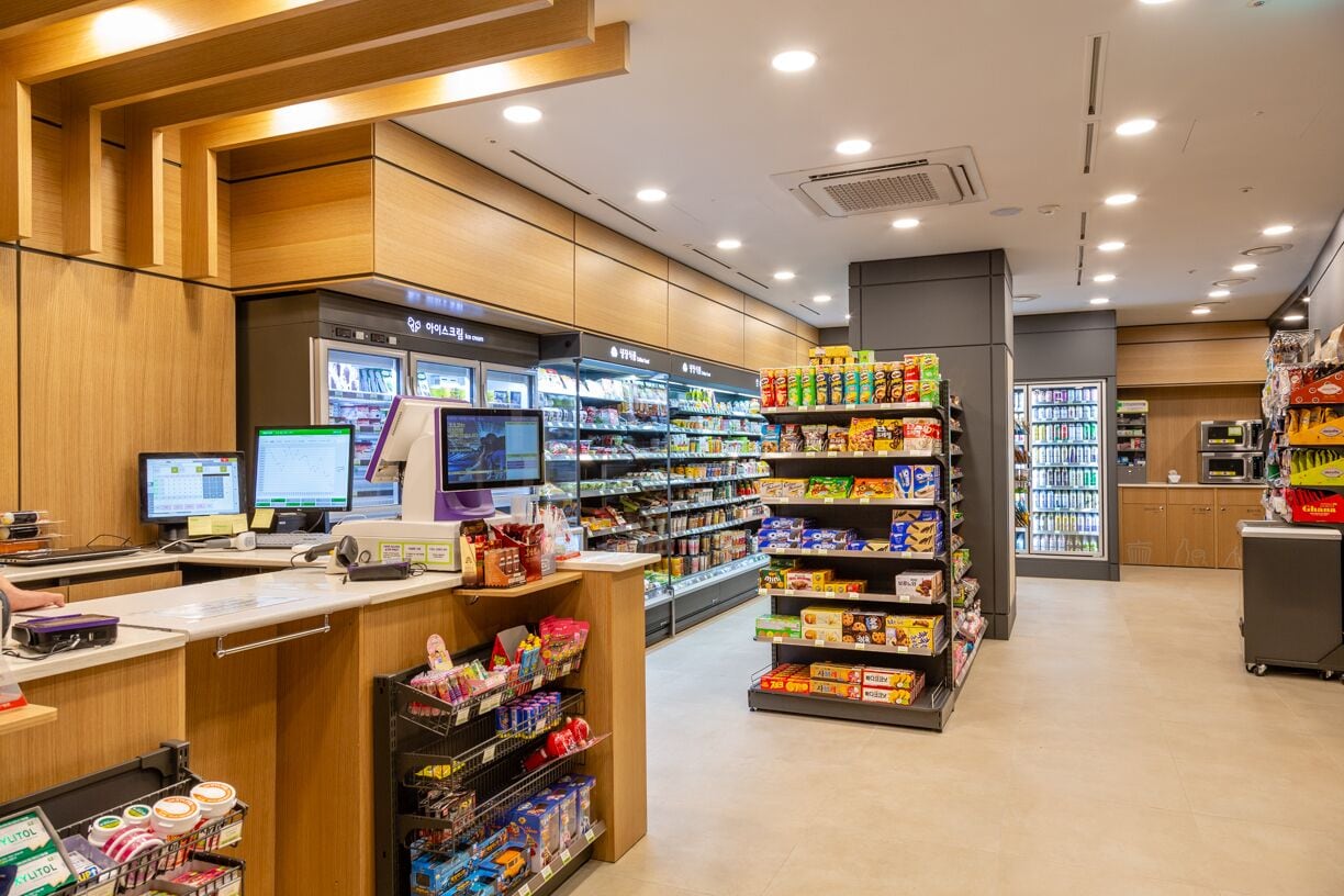 A grocery store interior with a checkout counter, refrigerated sections, and shelves stocked with various products.