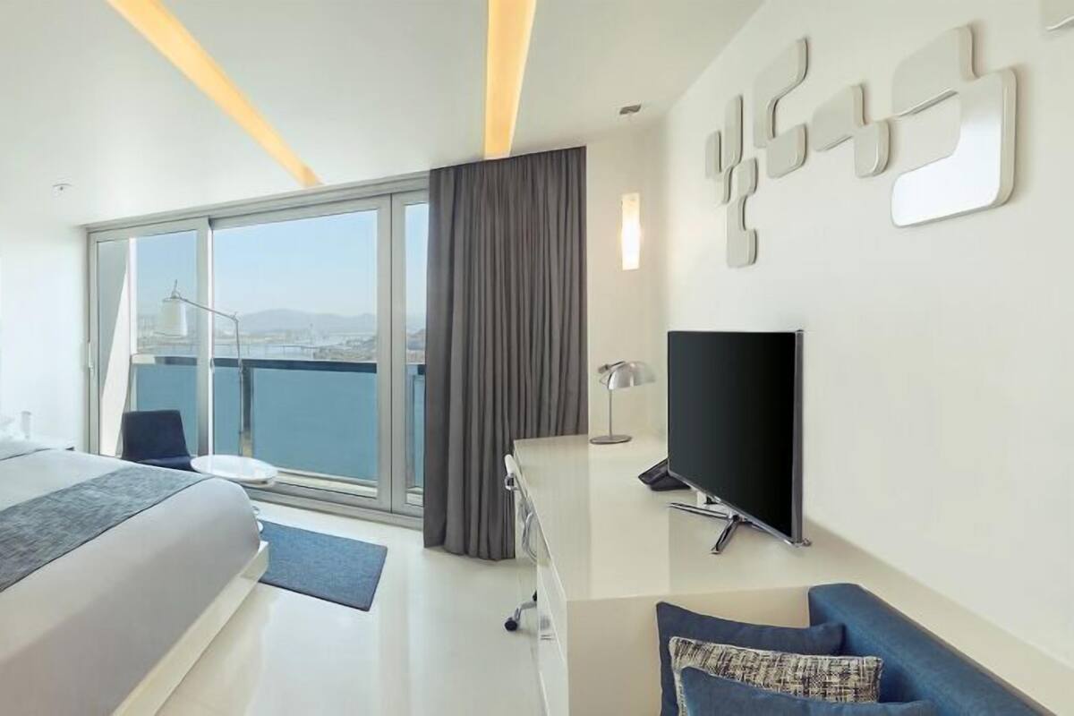 Een moderne hotelkamer met een groot bed, een televisie, een bureau en een balkon met uitzicht over de stad.