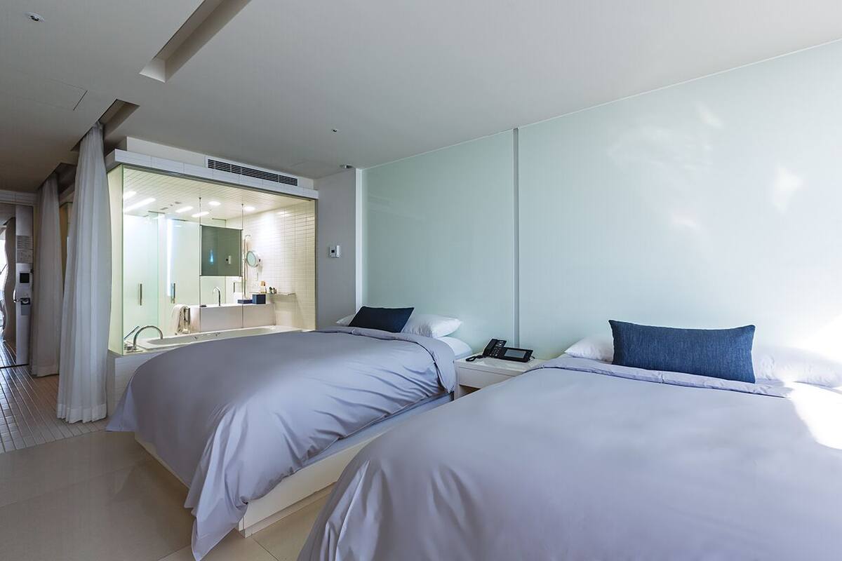 Een moderne hotelkamer met twee bedden, een badkamer met een douchecabine van glas en een grote spiegel.