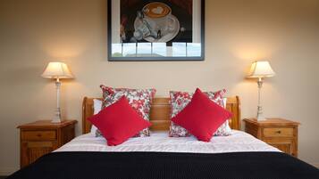 A neatly made bed with red and floral pillows, two bedside tables with lamps, and a framed artwork above the bed.