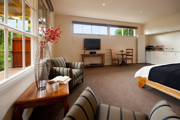 A bedroom with a bed, a desk, a TV, and a seating area with chairs and a table. - Daylesford House Studio (Daylesford)
