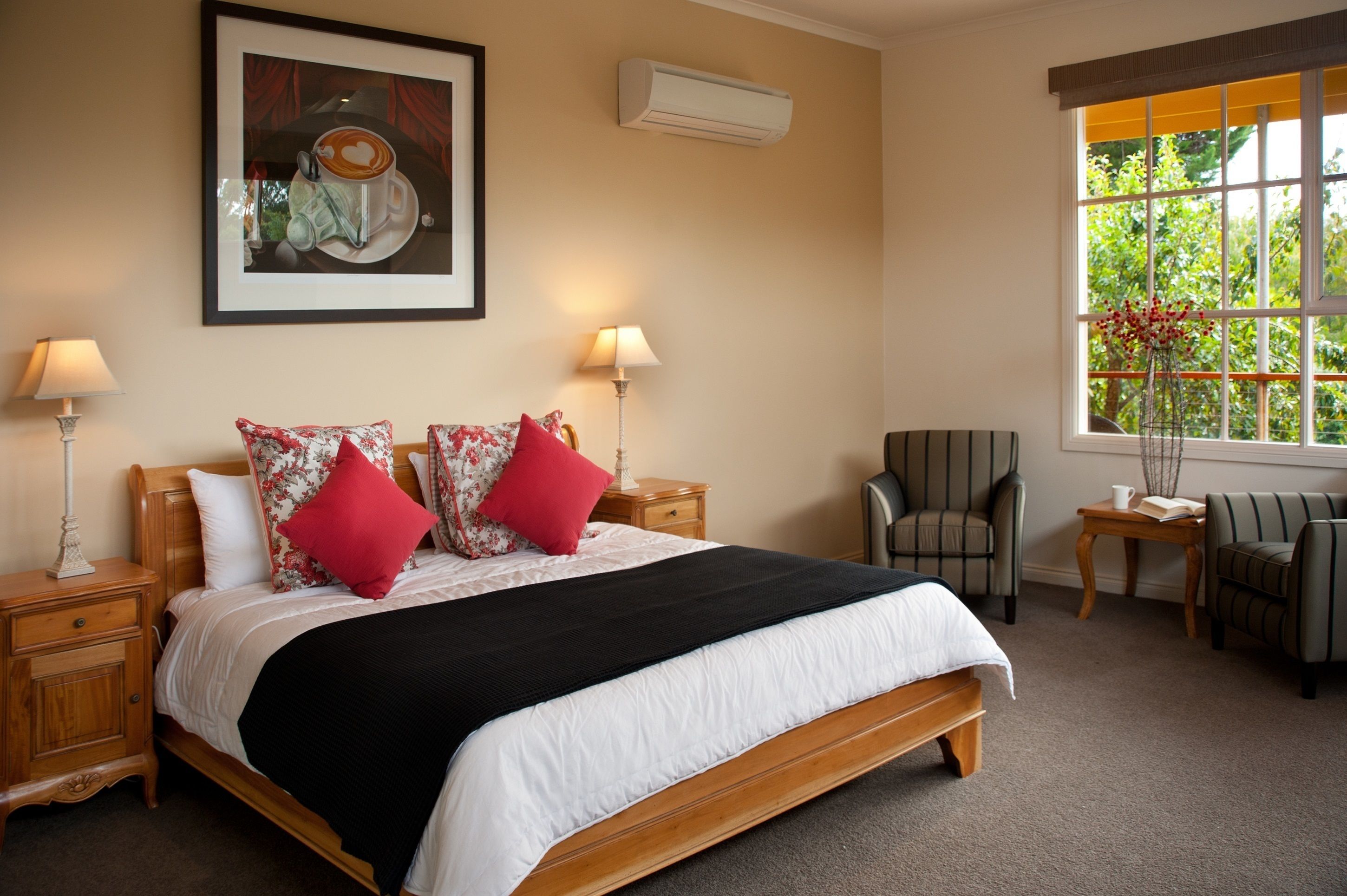 A neatly arranged bedroom with a large bed, two bedside tables with lamps, a chair, and a window with a view of greenery.