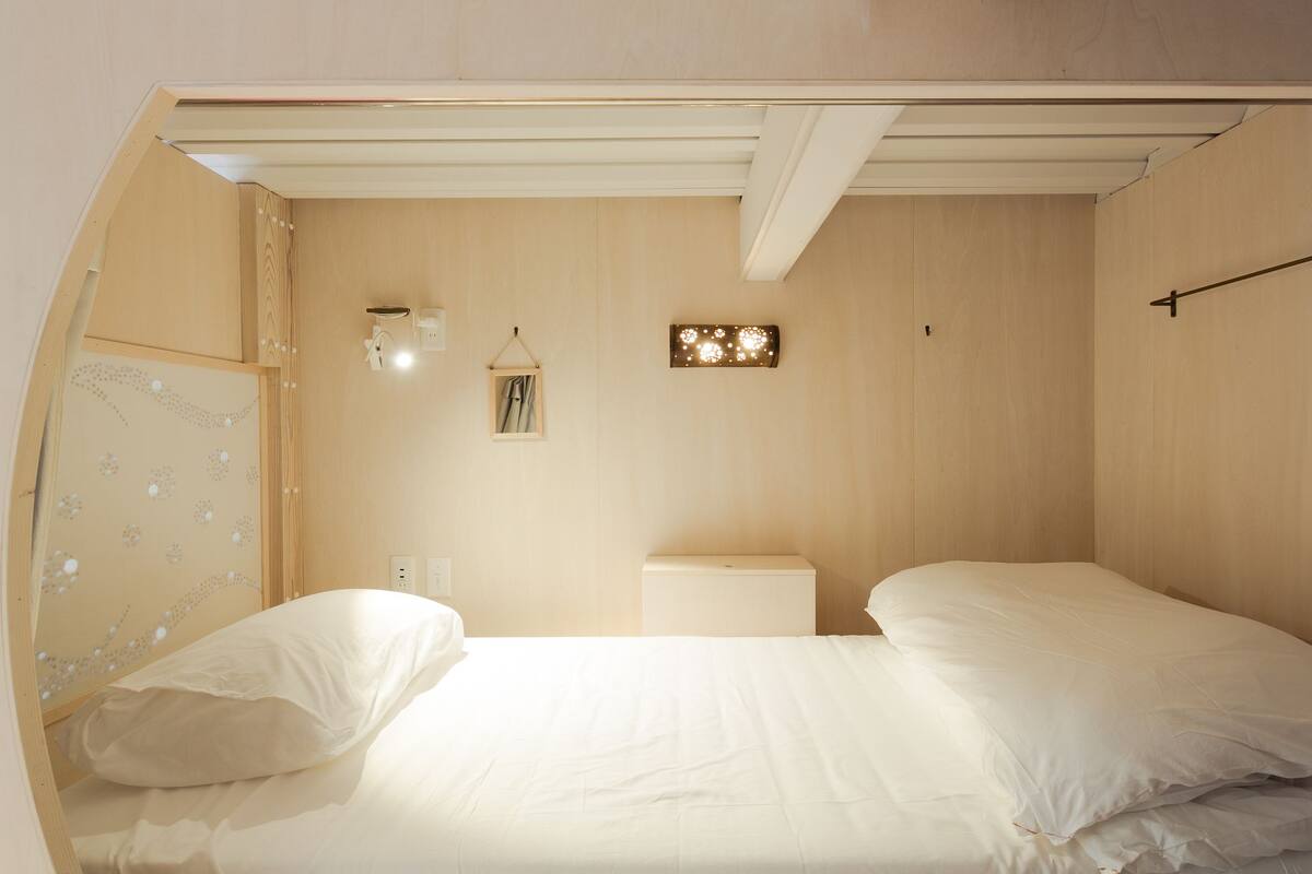 A bedroom with a bunk bed, a bedside table, a wall-mounted light, and a small mirror.