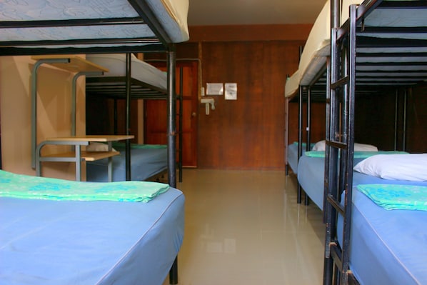A dormitory room with bunk beds, a desk, and a door with a sign.
