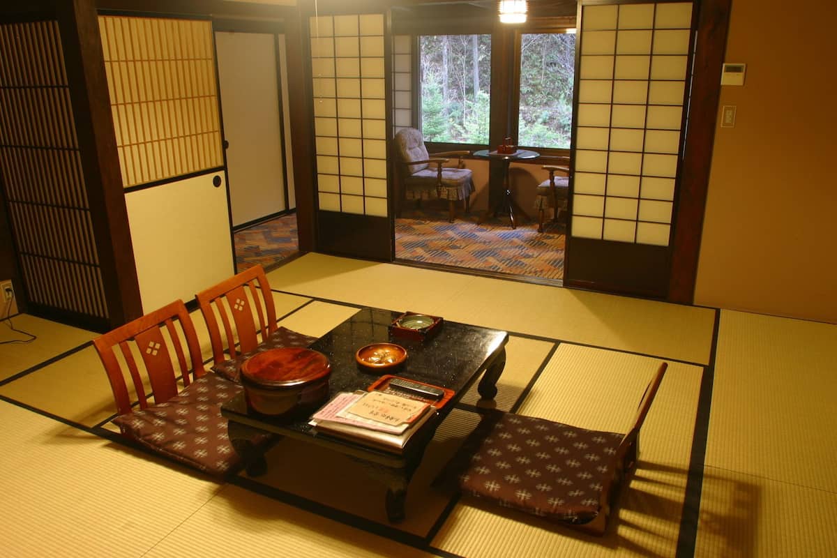 Una habitación japonesa tradicional con suelo de tatami, una mesa baja con un juego de té y vistas al bosque a través de puertas correderas.
