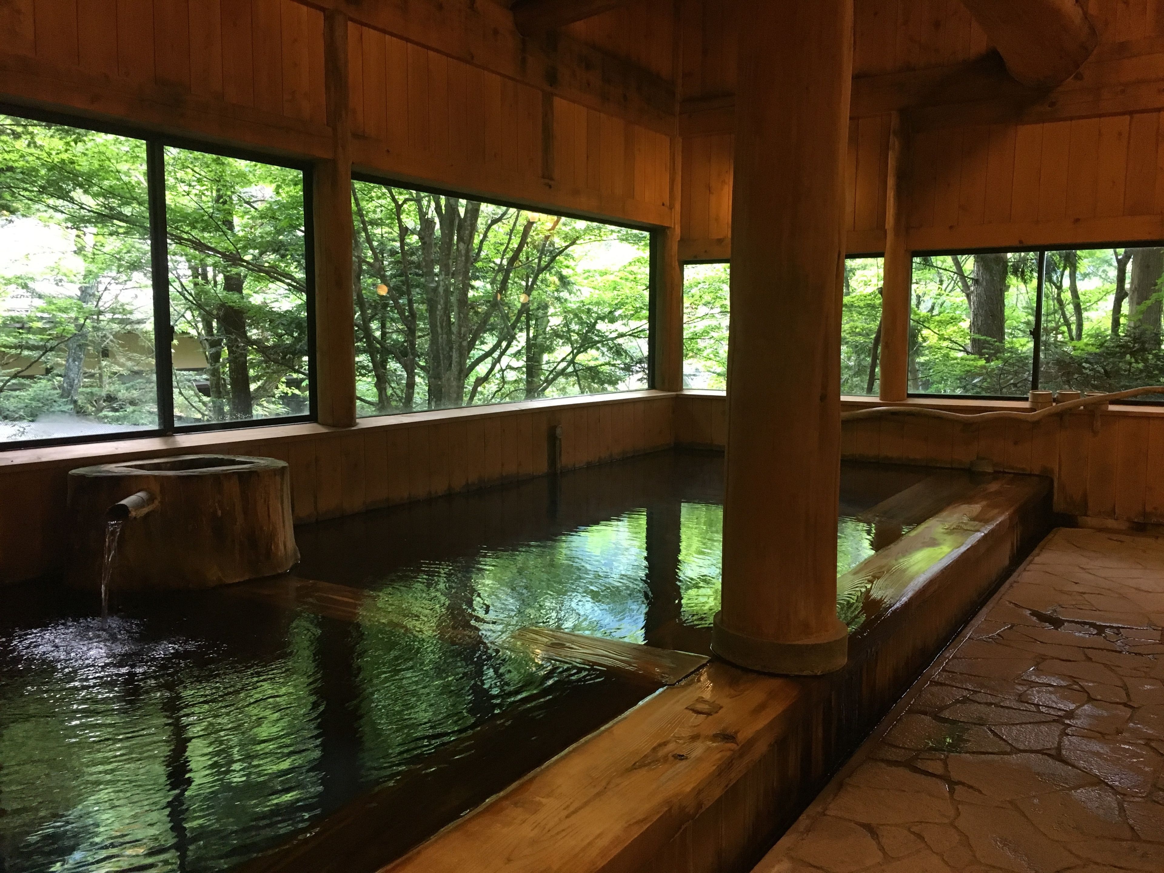 Una bañera de madera tradicional con suelo de madera y ventanas amplias con vistas a una zona boscosa.