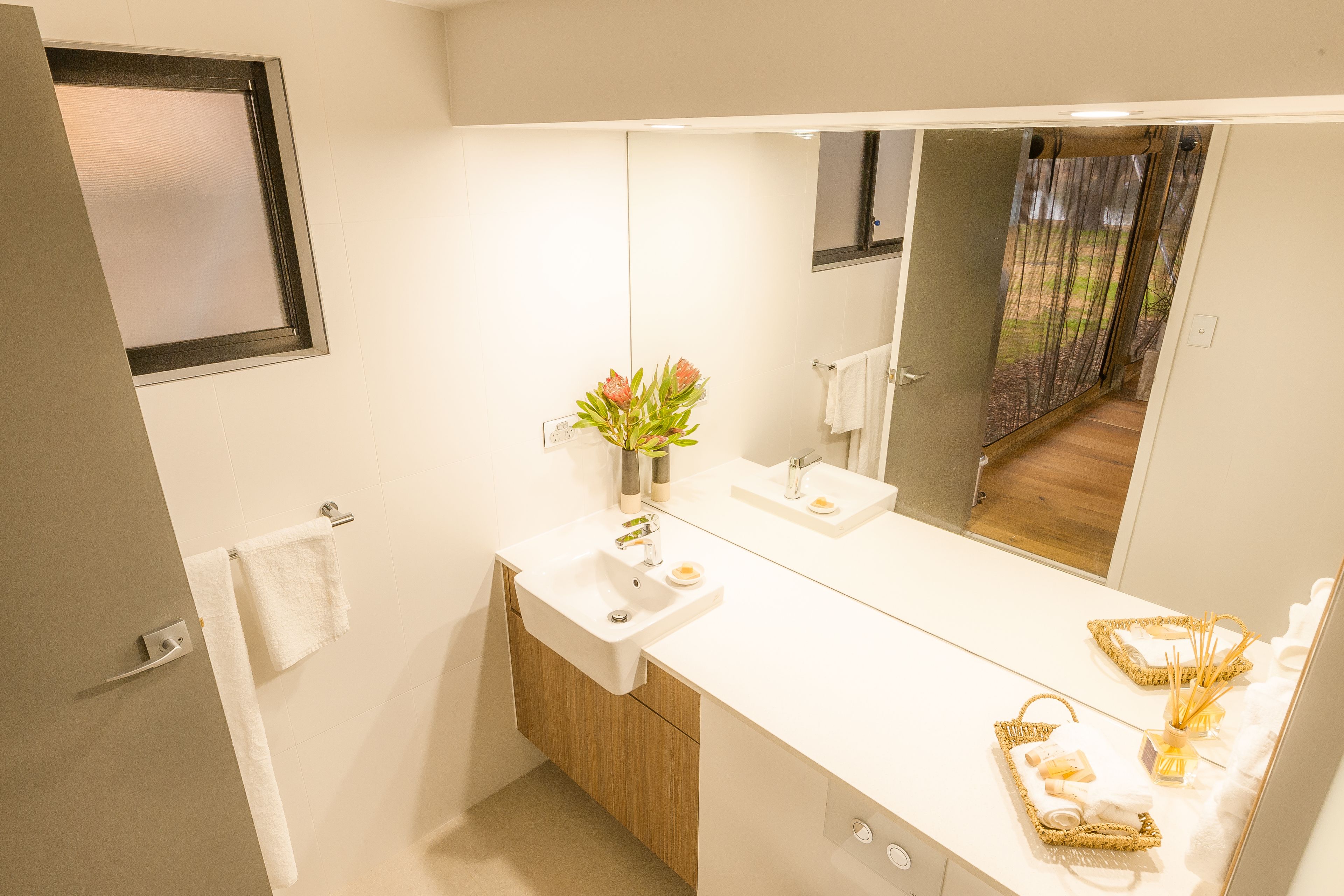 A modern bathroom with a large mirror, white sink, and wooden cabinet.