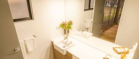 A modern bathroom with a large mirror, white sink, and wooden cabinet.