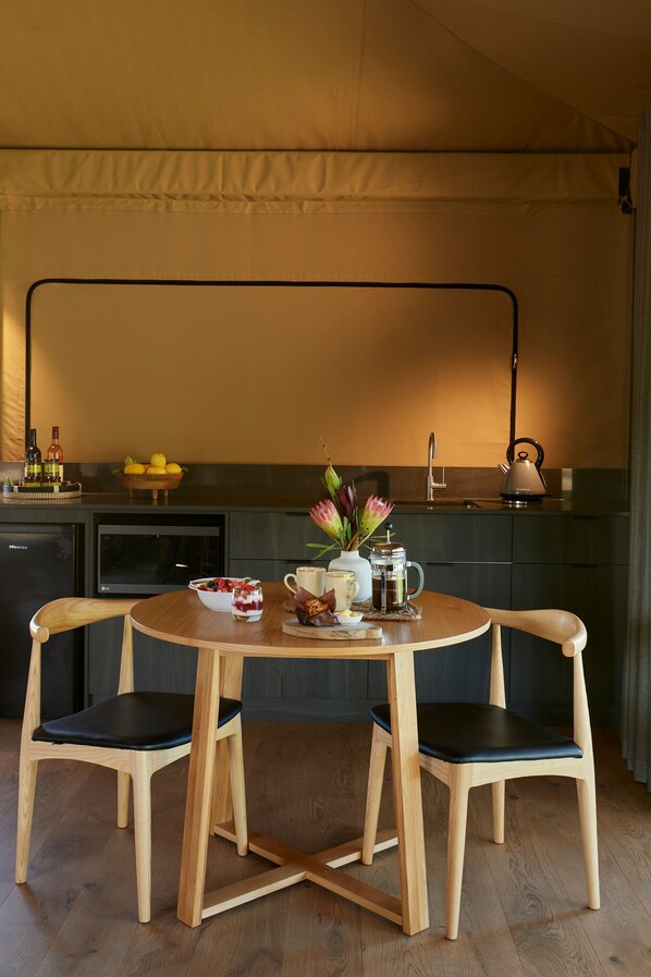 A compact kitchen with a dining area, equipped with a kettle, a bowl of fruit, and a coffee maker. - Olio Bello Lakeside Glamping (Cowaramup)