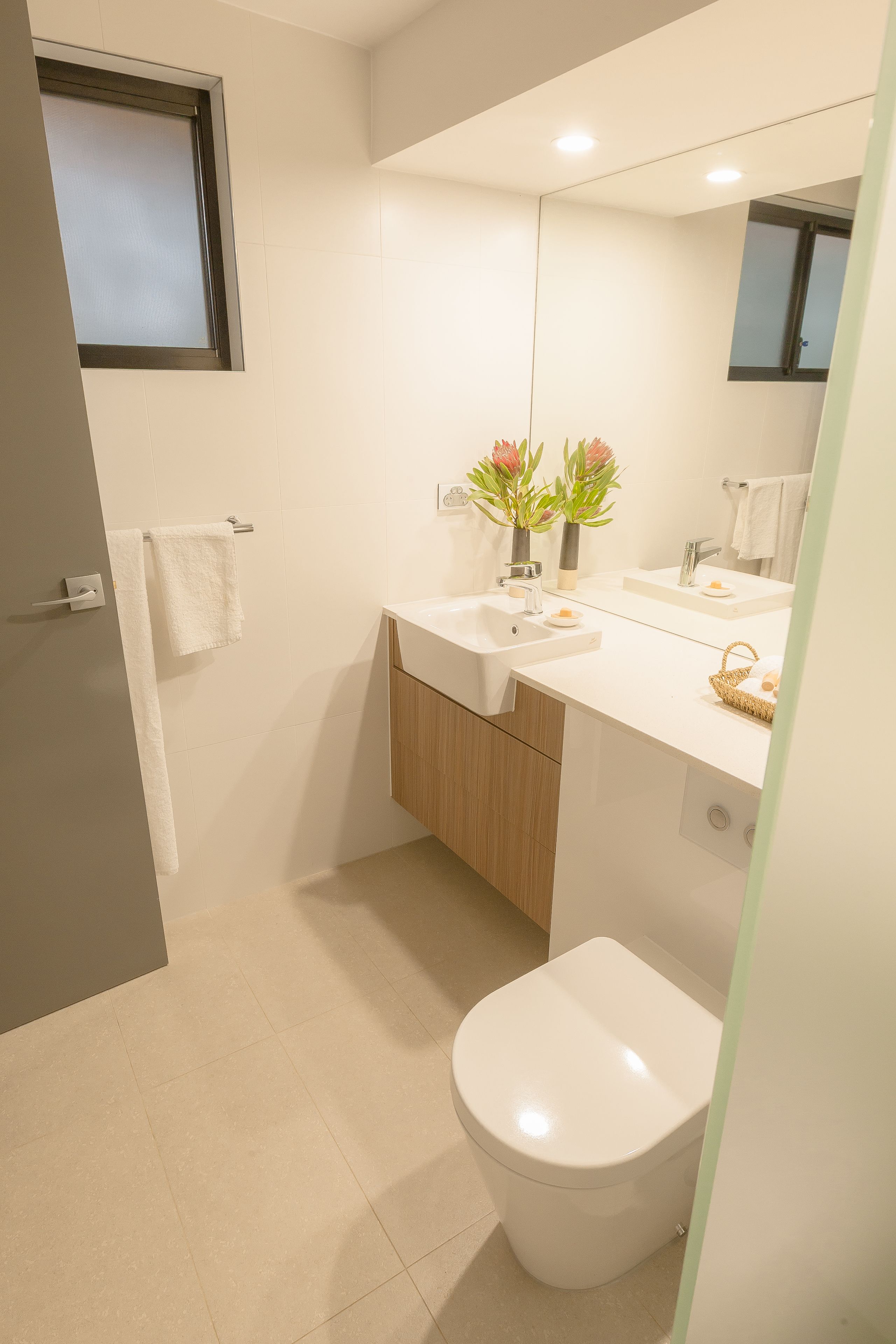 Un bagno moderno con servizi igienici, lavandino e specchio. Asciugamani appesi a un porta-asciugamani e una finestra sopra il lavandino.