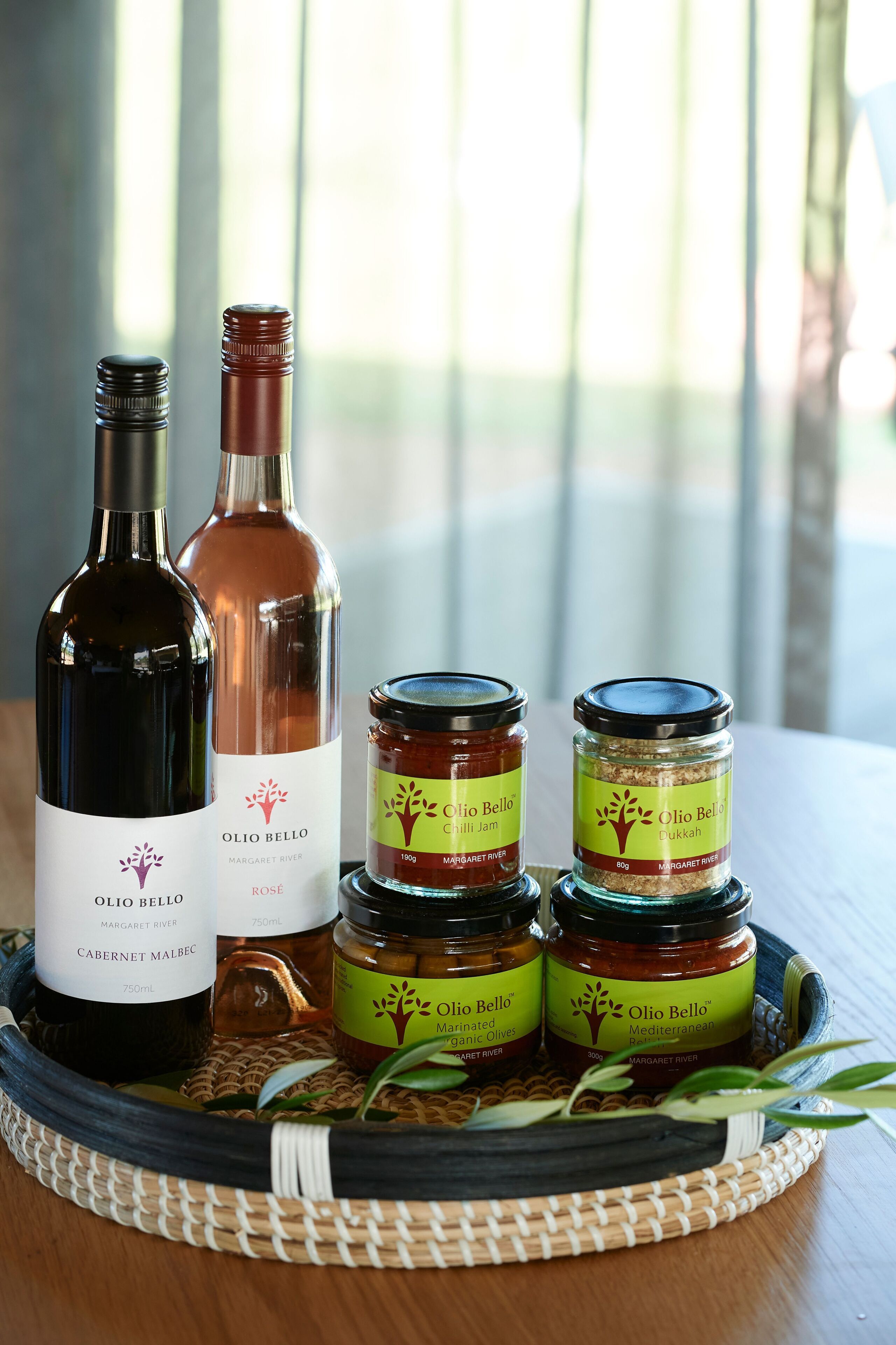 A bottle of Olio Bello Cabernet Malbec and a bottle of Olio Bello Dukkah on a tray with jars of Olio Bello Dukkah and Chilli Jam.