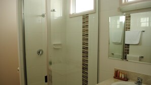A bathroom with a glass shower enclosure, a sink with a mirror above it, and toiletries on the counter. - The David Motel (Berserker)