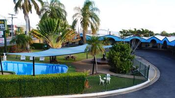 Un área de piscina con valla, palmeras y un edificio con tejados azules.
