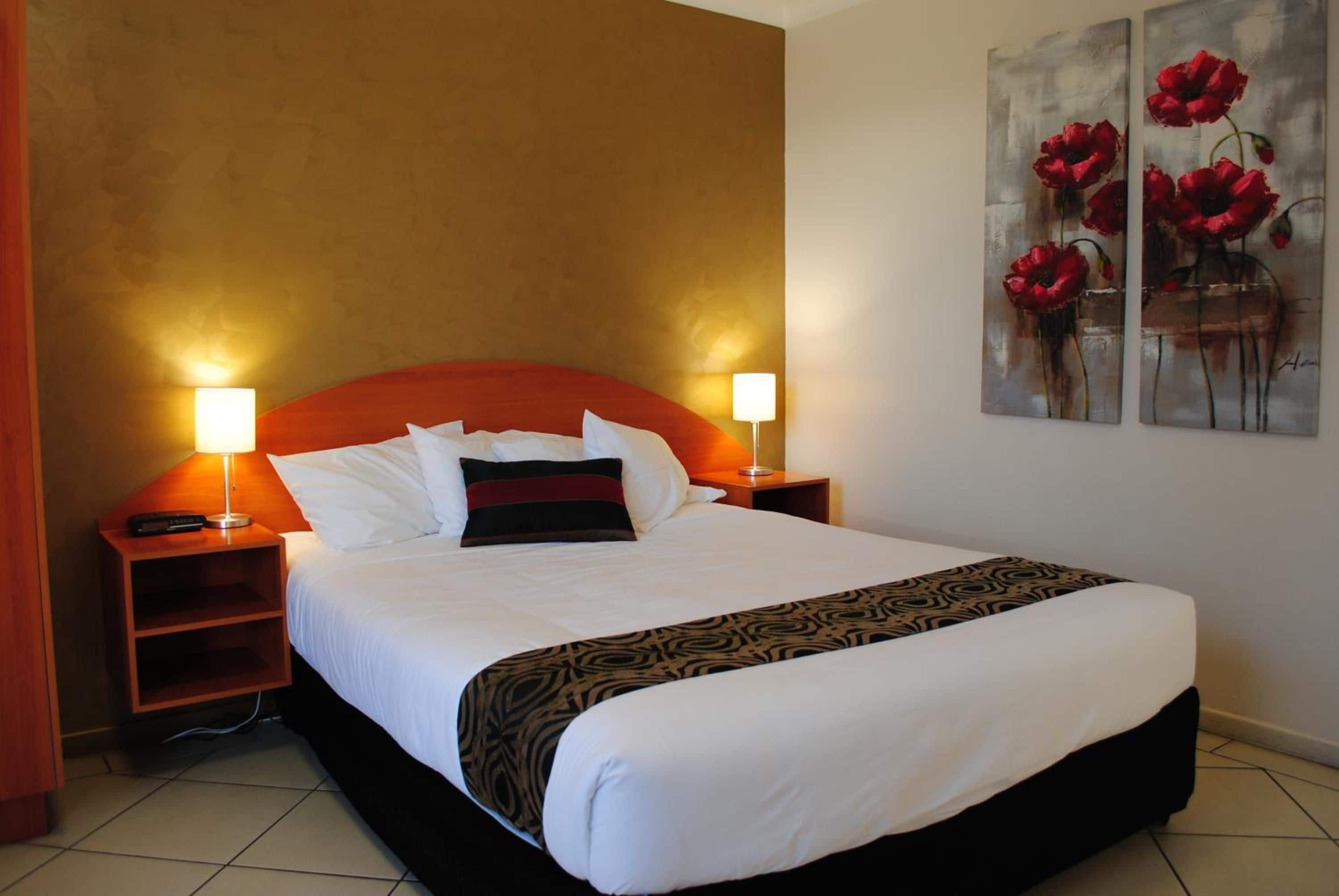 A hotel room with a large bed, two bedside tables, a nightstand, and a painting on the wall.