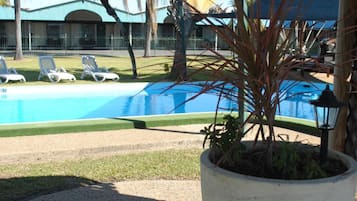 A pool area with lounge chairs, a large planter with a plant, and a building in the background.