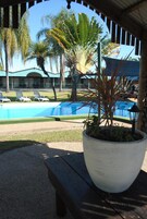 Uma área de piscina com espreguiçadeiras, um grande vaso com uma planta e um edifício ao fundo.