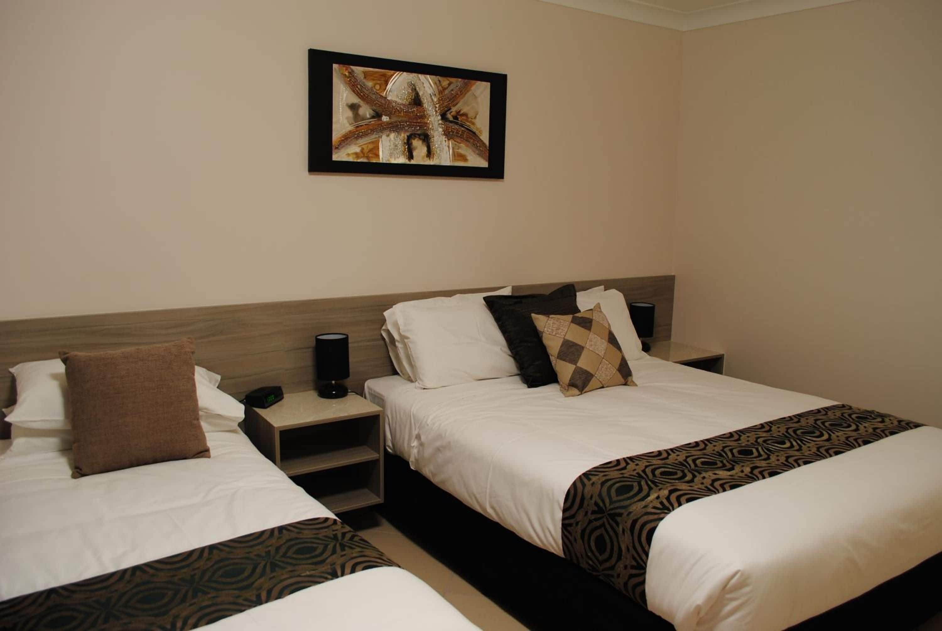 Una habitación de hotel con dos camas, una mesita de noche con una lámpara y un cuadro en la pared.