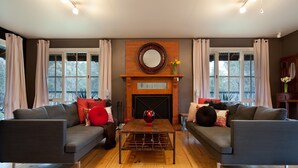 A living room with two grey sofas, a wooden coffee table, a fireplace, and large windows with curtains. - Finlie (Hepburn)