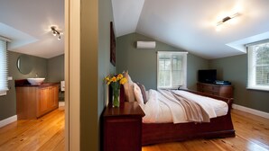 A bedroom with a wooden floor, a bed with a white comforter, a dresser, a vanity with a mirror, and a television on a stand. - Finlie (Hepburn)