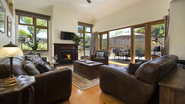 A spacious living room with leather sofas, a fireplace, and large windows offering a view of the backyard.