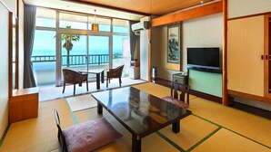 A room with a large table, chairs, a TV, and a view of the sea.