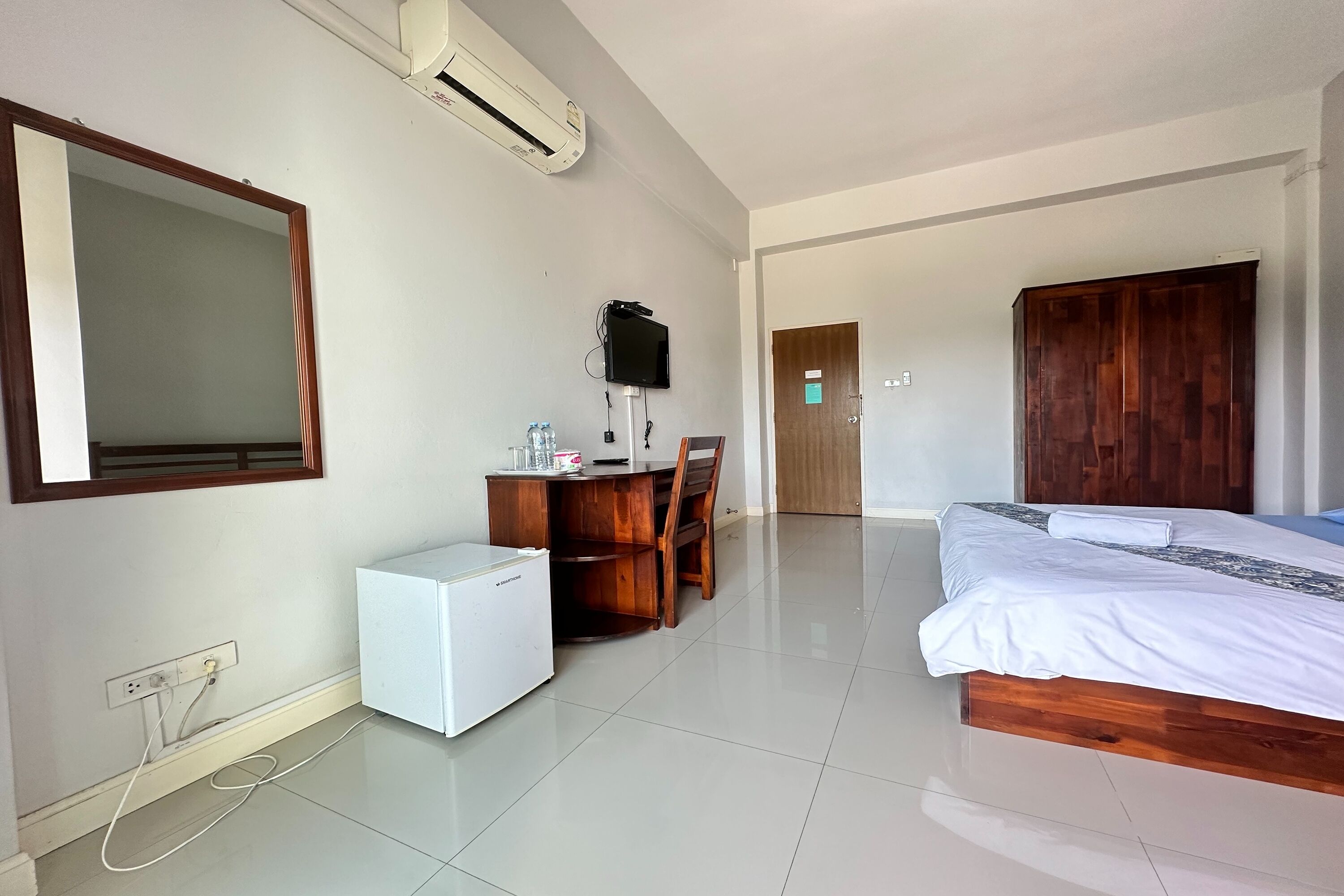 A hotel room with a bed, desk, and chair, an air conditioner, and a TV.