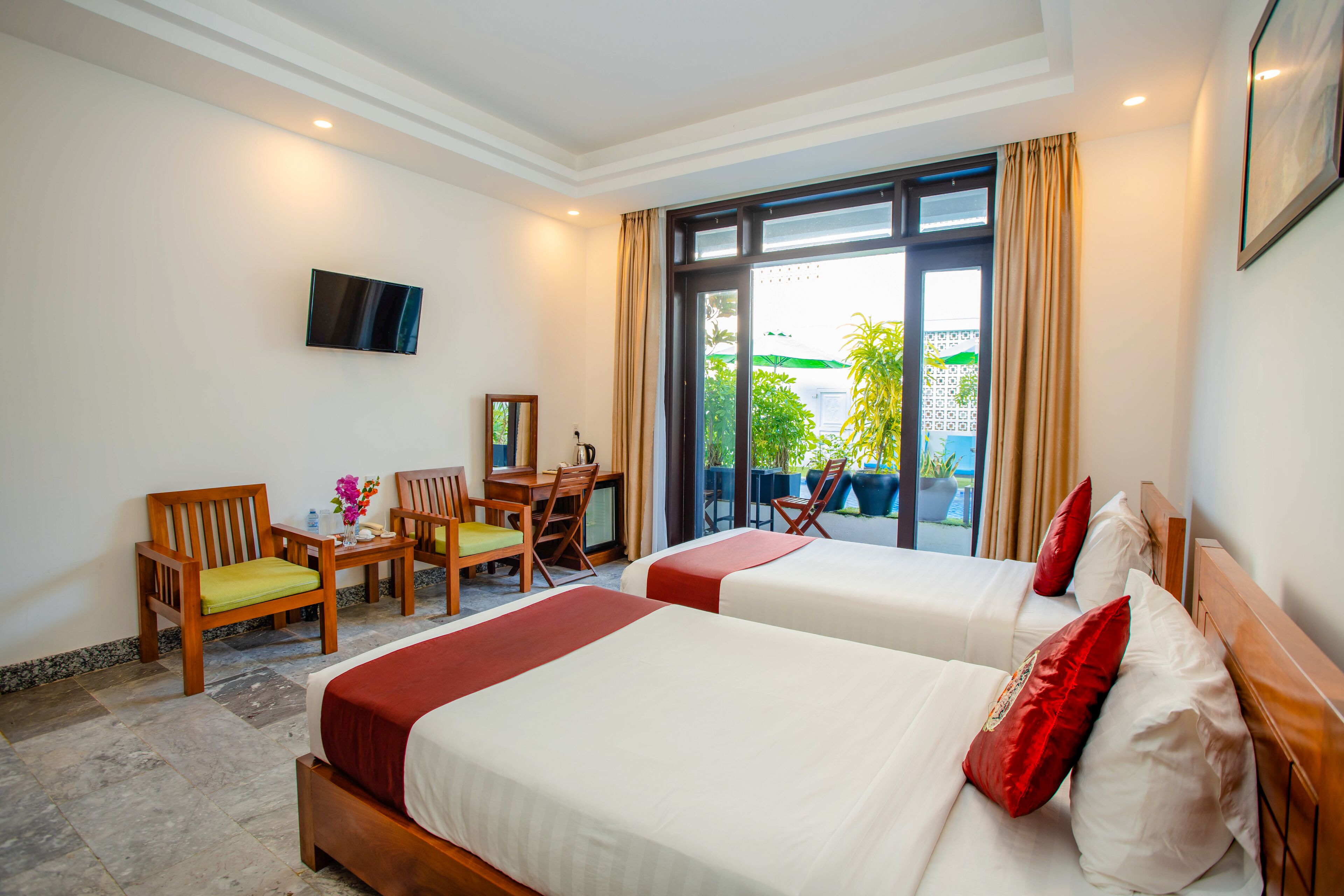 A hotel room with two beds, a desk, chairs, and a TV.