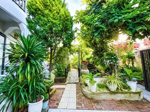Een tuinpad dat leidt naar een poort, omringd door verschillende plantenpotten en groen.