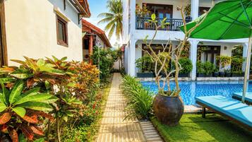 Un espace aménagé au bord de la piscine, avec un chemin pavé, des plantes en pot et des chaises longues.