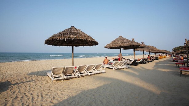 A beach with rows of sun loungers and thatched umbrellas. - Trendy Life Villa Hoi An (Da Nang)