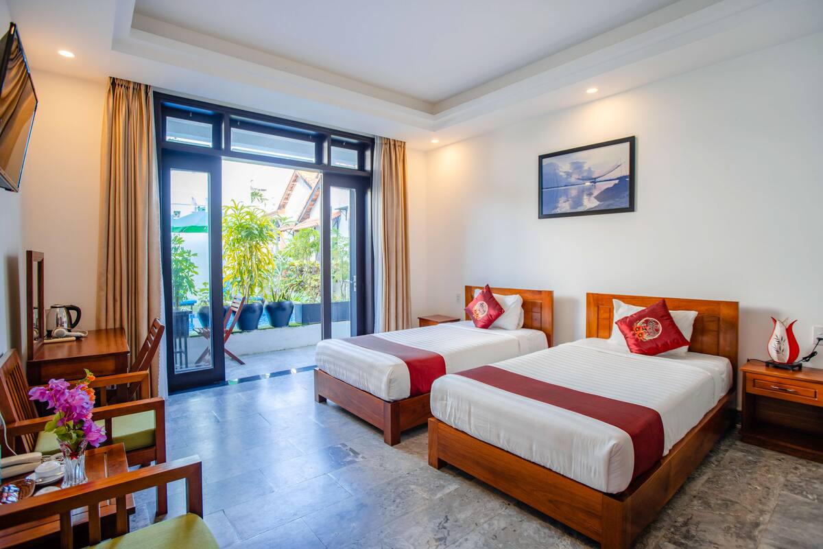 Ein Hotelzimmer mit zwei Betten, einem Schreibtisch, Stühlen, einer Kaffeemaschine und Blick ins Freie.