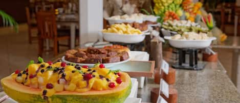 A buffet with various dishes, including a large melon bowl topped with fruit and berries, and other food items in the background.