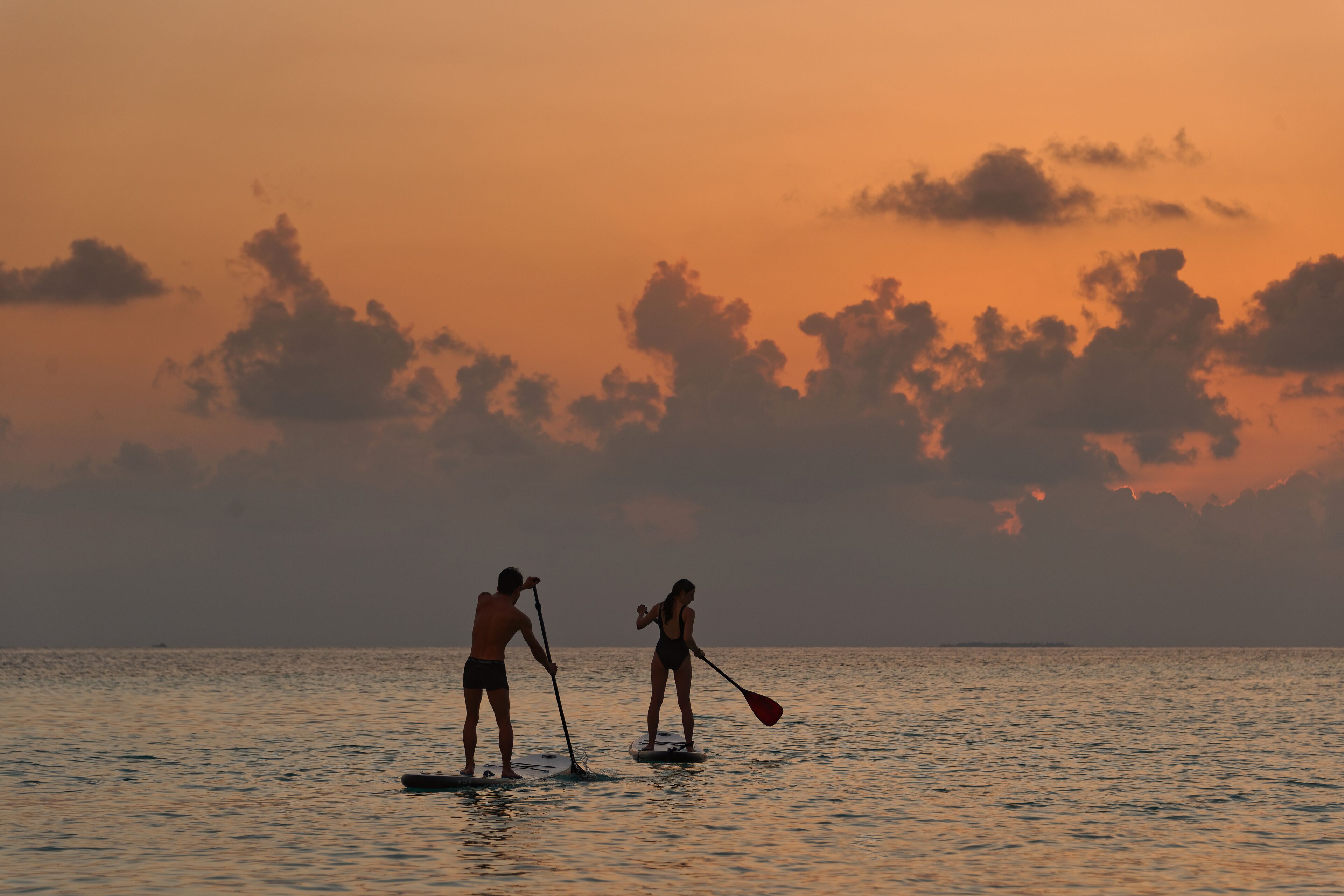 Dos personas haciendo paddleboard en un mar tranquilo al atardecer.