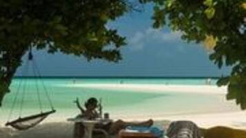A beach scene with a hammock, a table, and a chair under a tree.