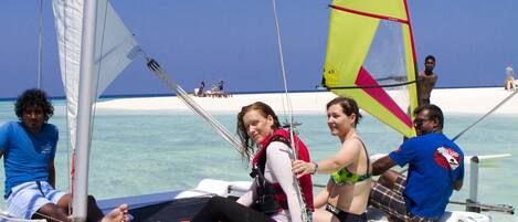 Un velero con pasajeros, agua turquesa cristalina y una playa arenosa al fondo.