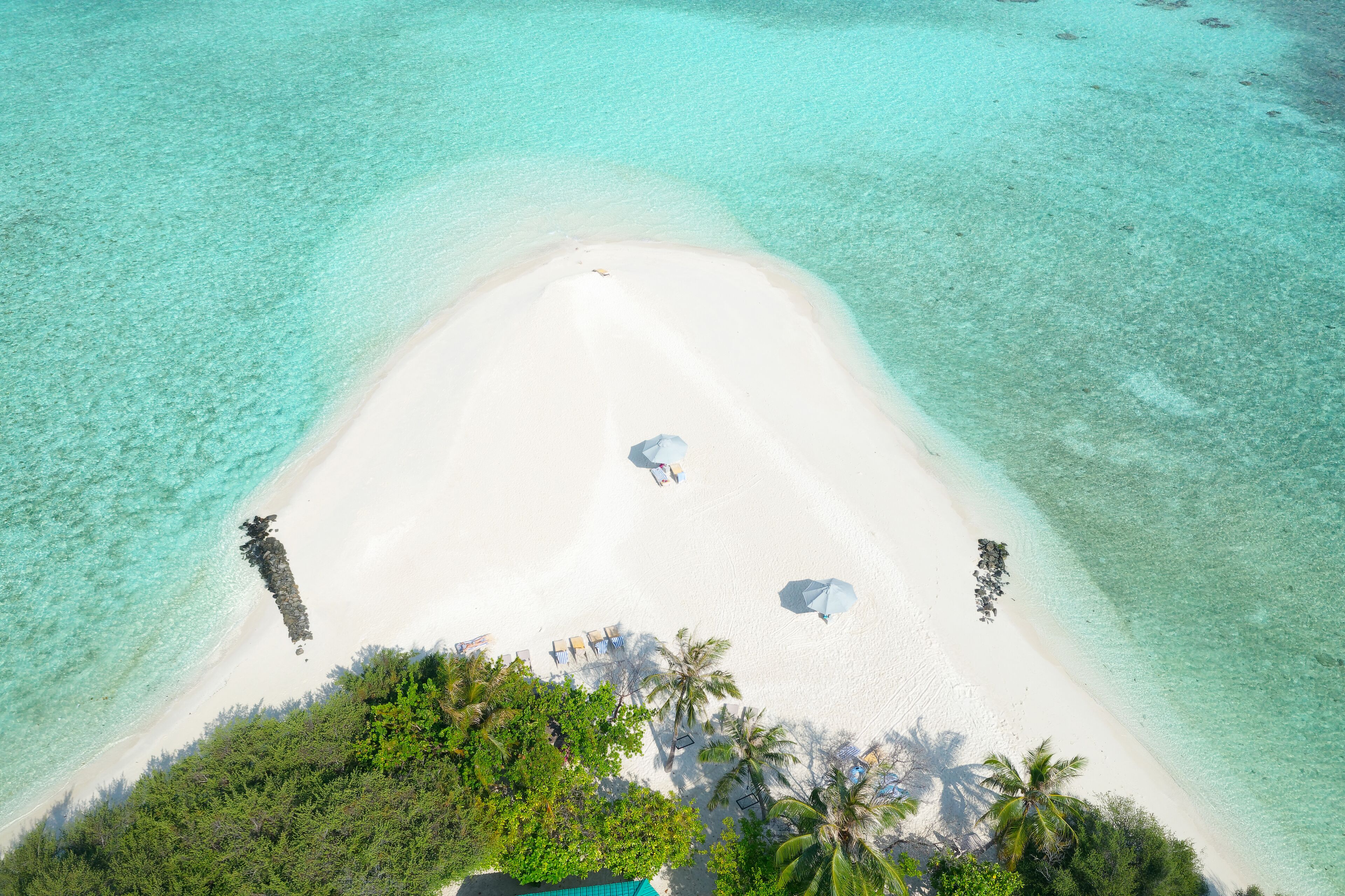 Vista aérea de una playa con agua turquesa cristalina, arena blanca y algunas sombrillas.
