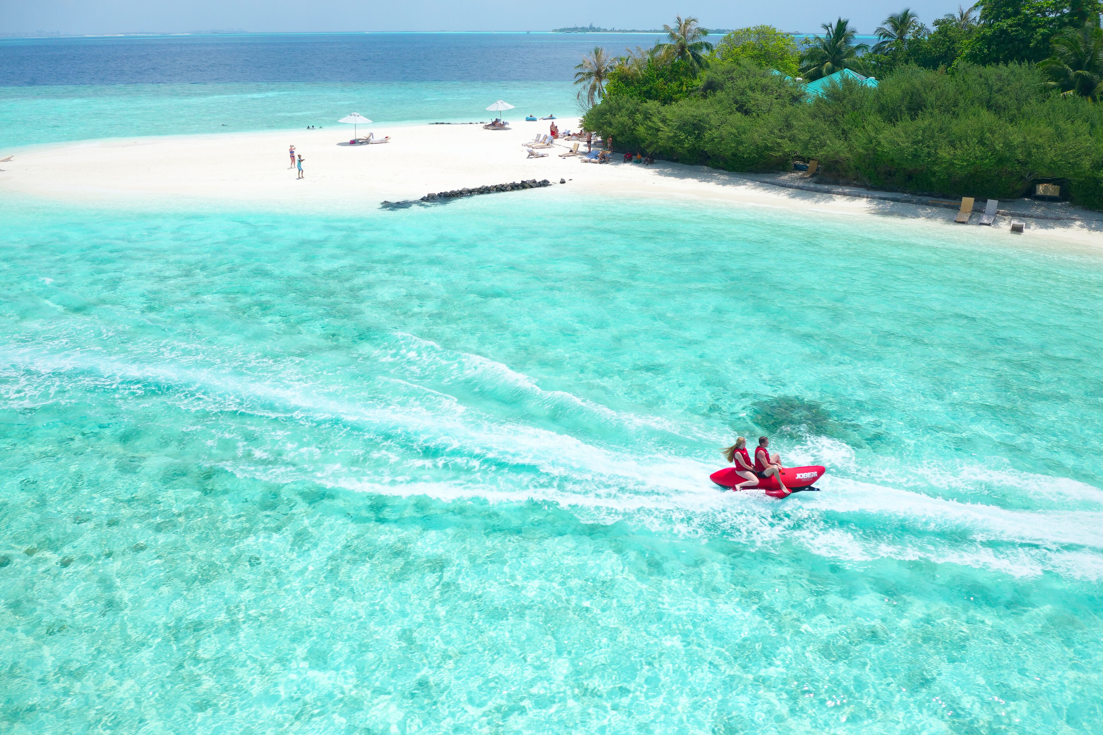 A beach with clear turquoise water, a white sandy shore, and a few people enjoying the area.