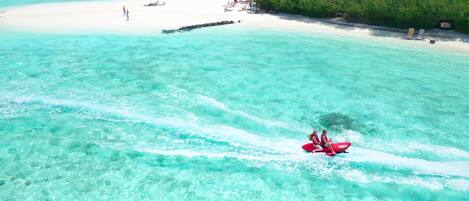 A beach with clear turquoise water, a white sandy shore, and a few people enjoying the area.