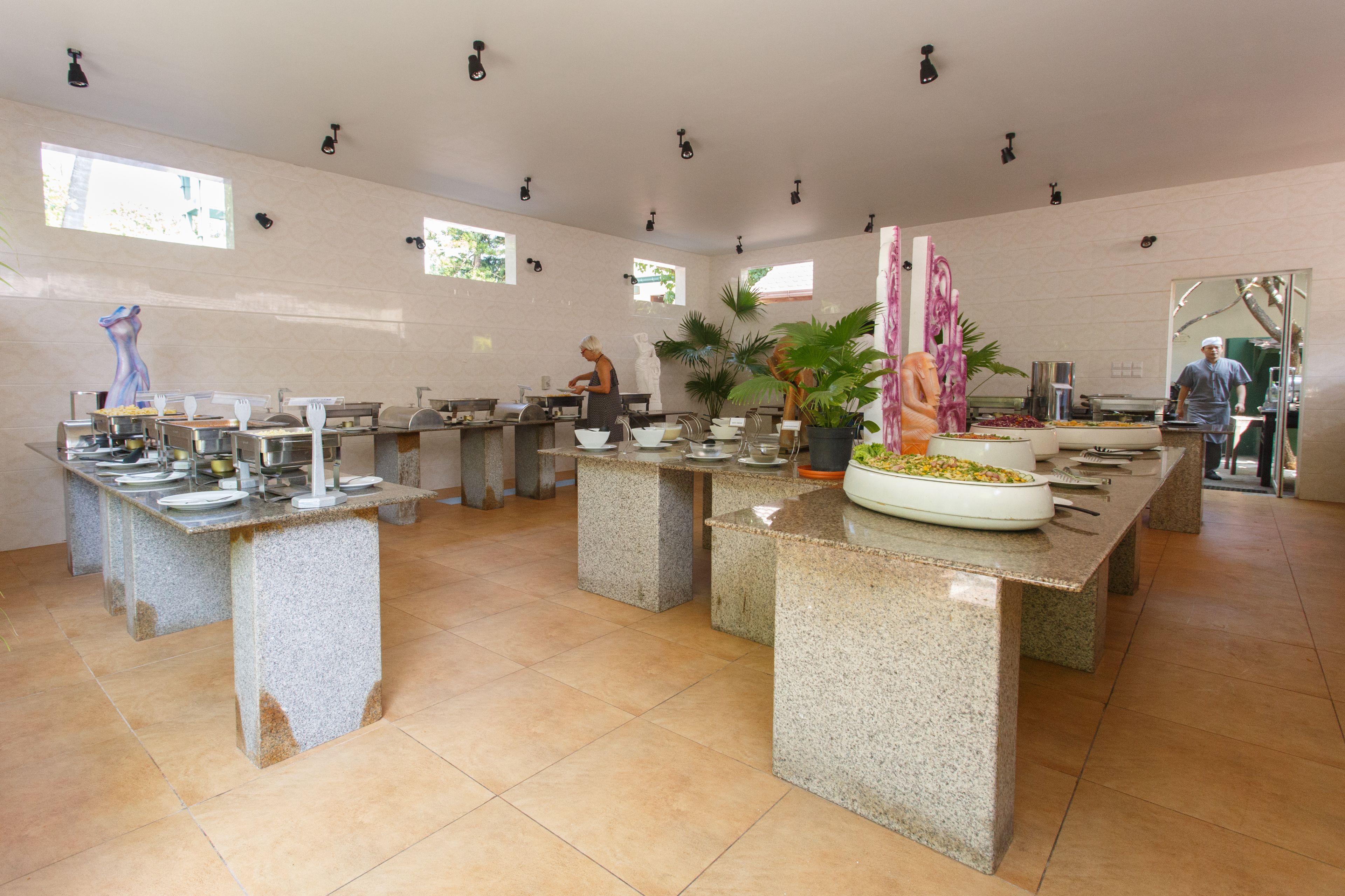Un vaste espace dédié à la salle à manger, avec de nombreuses tables en granit, chacune étant agrémentée d’une variété d’assiettes et de couverts.