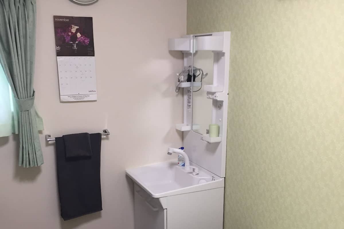 A small, clean bathroom with a white sink, a mirror, a clock, and a calendar.
