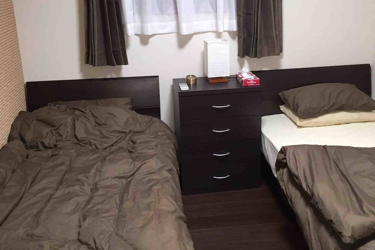 A bedroom with two beds, a nightstand with a lamp, and a window with curtains.