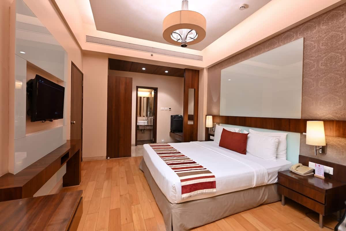A hotel room with a large bed, bedside lamps, a TV mounted on the wall, and a wooden floor.