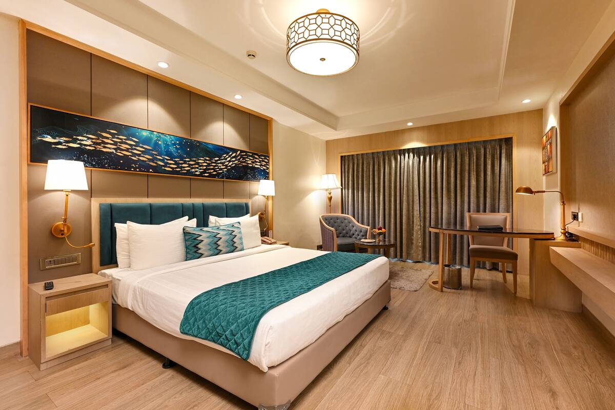 A modern hotel room with a large bed, a desk, a chair, and a painting on the wall.