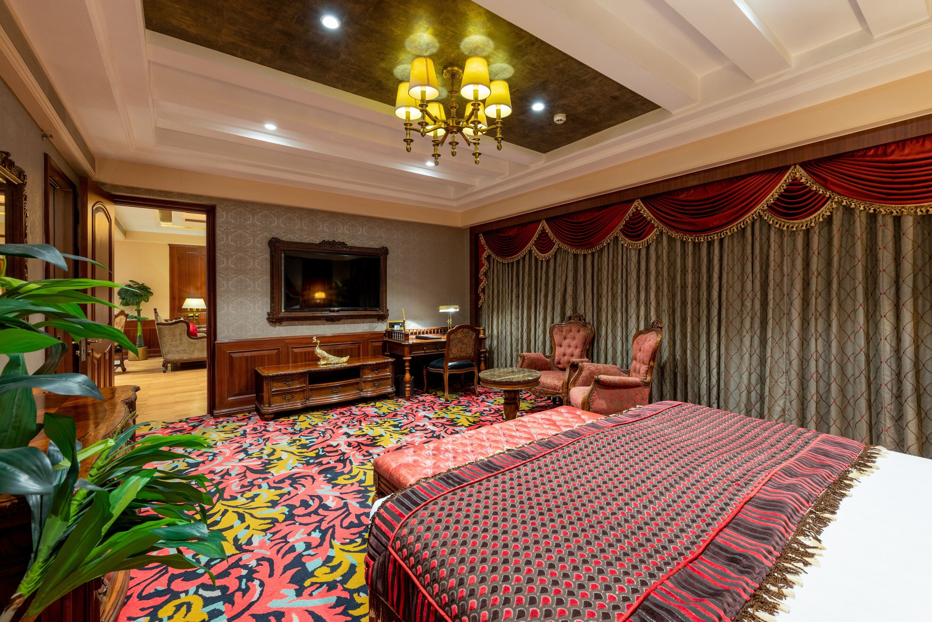A spacious bedroom with a large bed, a chandelier, a television, and a desk with a chair.