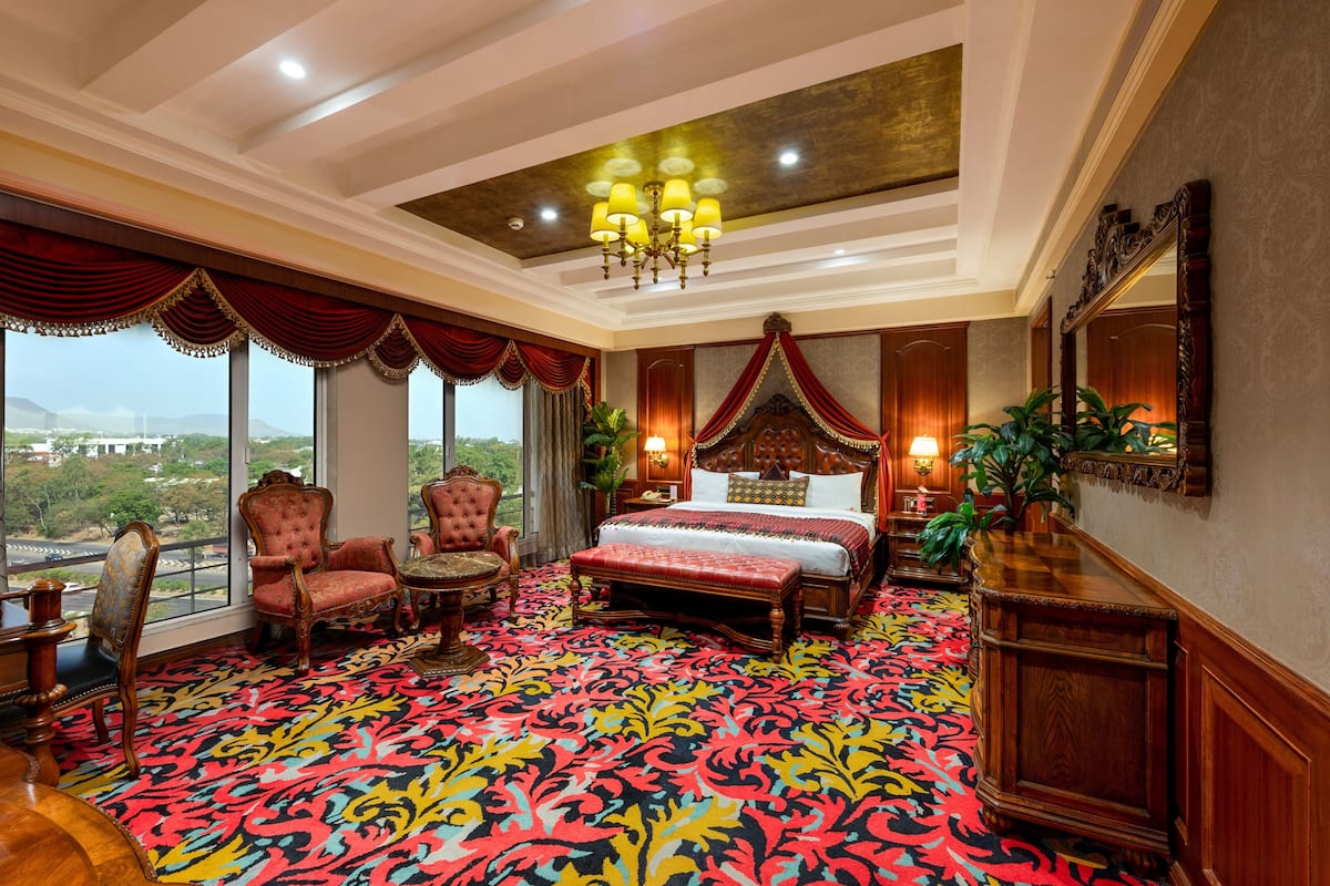 A spacious bedroom with a large bed, ornate curtains, and a view of the cityscape.