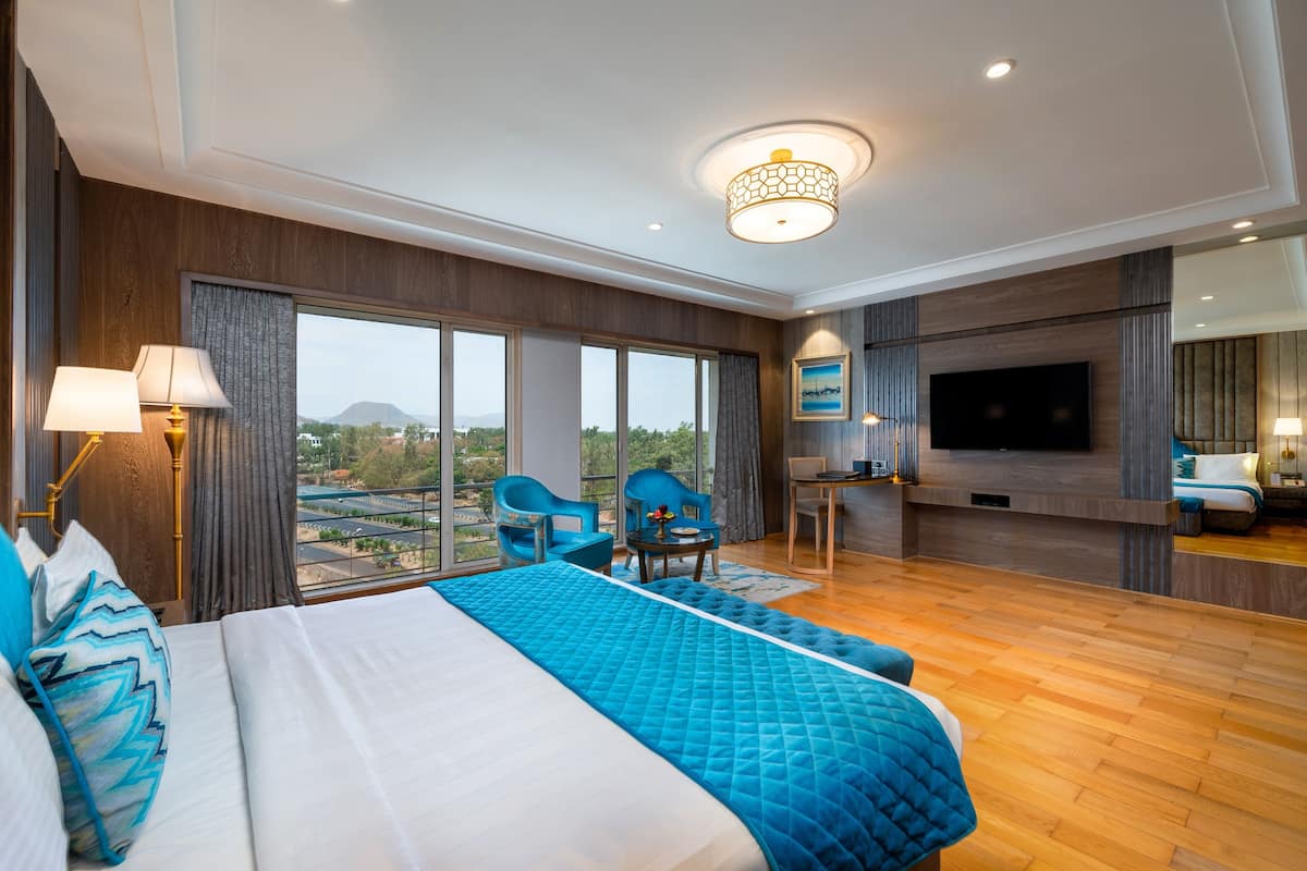 A modern hotel room with a large bed, a TV, and a balcony with a city view.