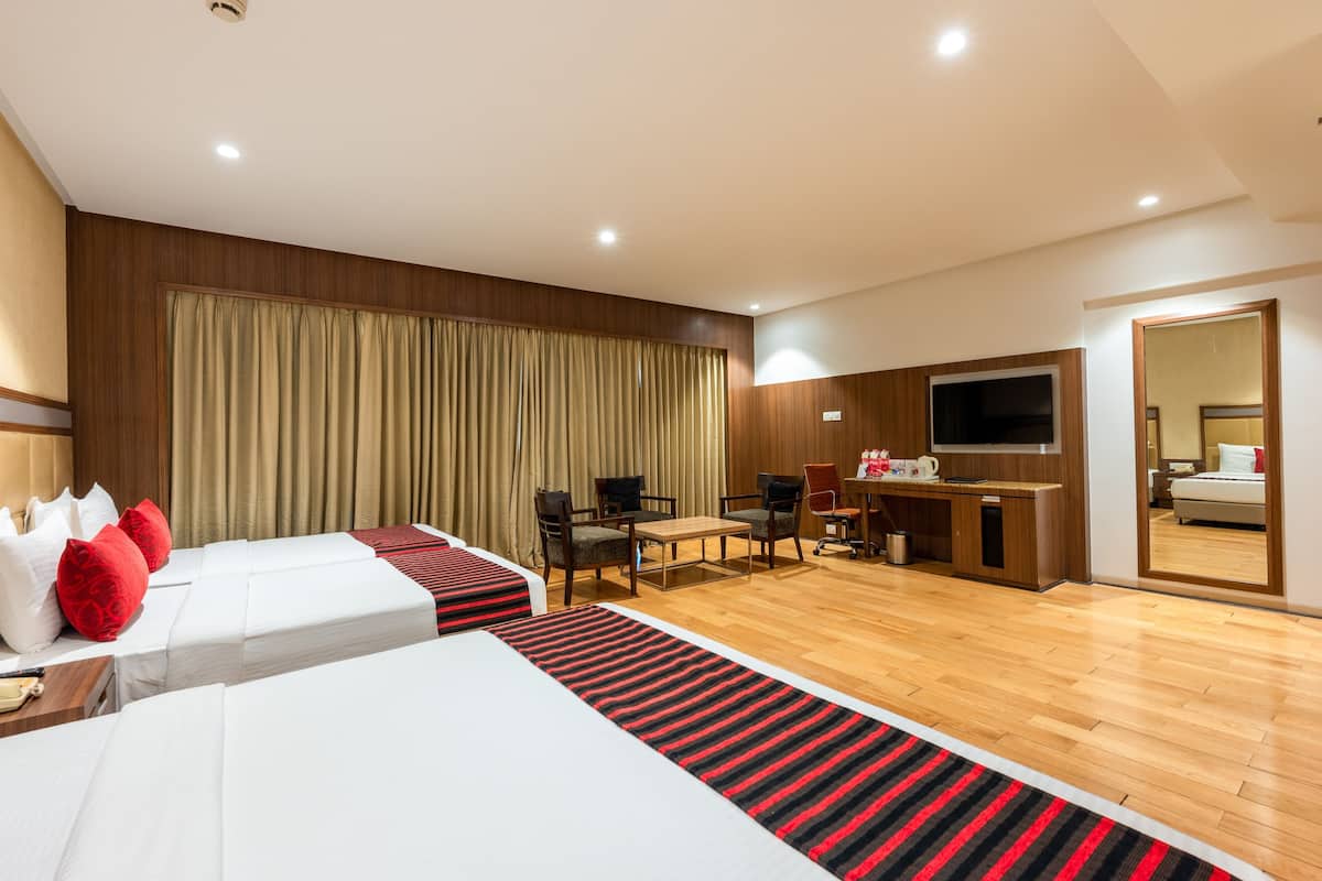 A hotel room with two beds, a desk, chairs, a TV, and a mirror.